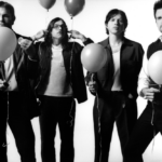 A black and white image of the members of Kings of Leon, four white men with brown hair, black pants, and black and white shirt and jacket combos. They are holding balloons but have serious facial expressions.