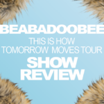 A baby blue background is covered by the edges of a light, tan-and-brown fur coat in the corners. In white, all uppercase letters, text reads: "Beabadoobee," "This Is How Tomorrow Moves Tour," and "Show Review."