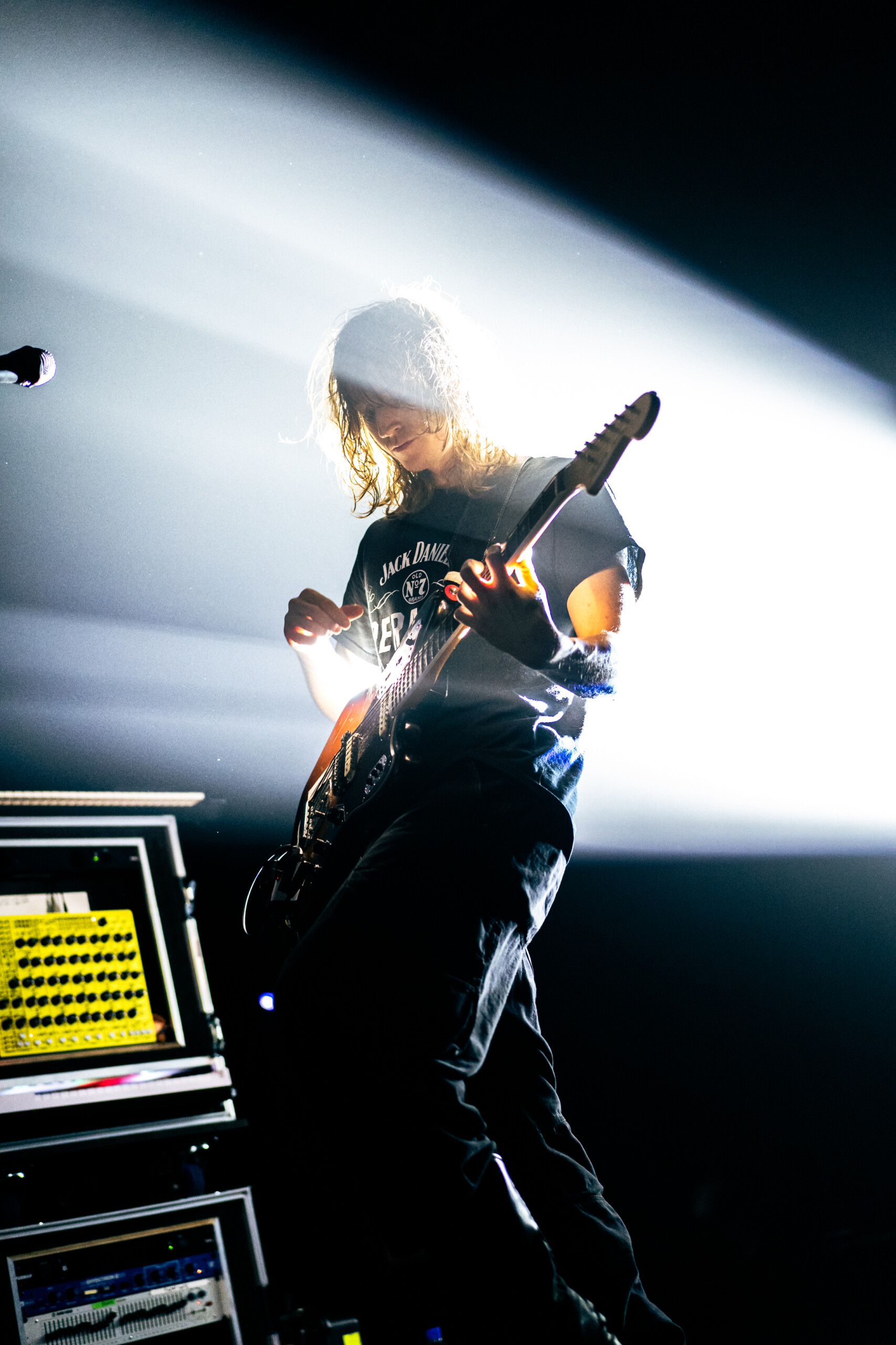 Mk.gee with a stage light behind him, strumming an electric guitar upwards.