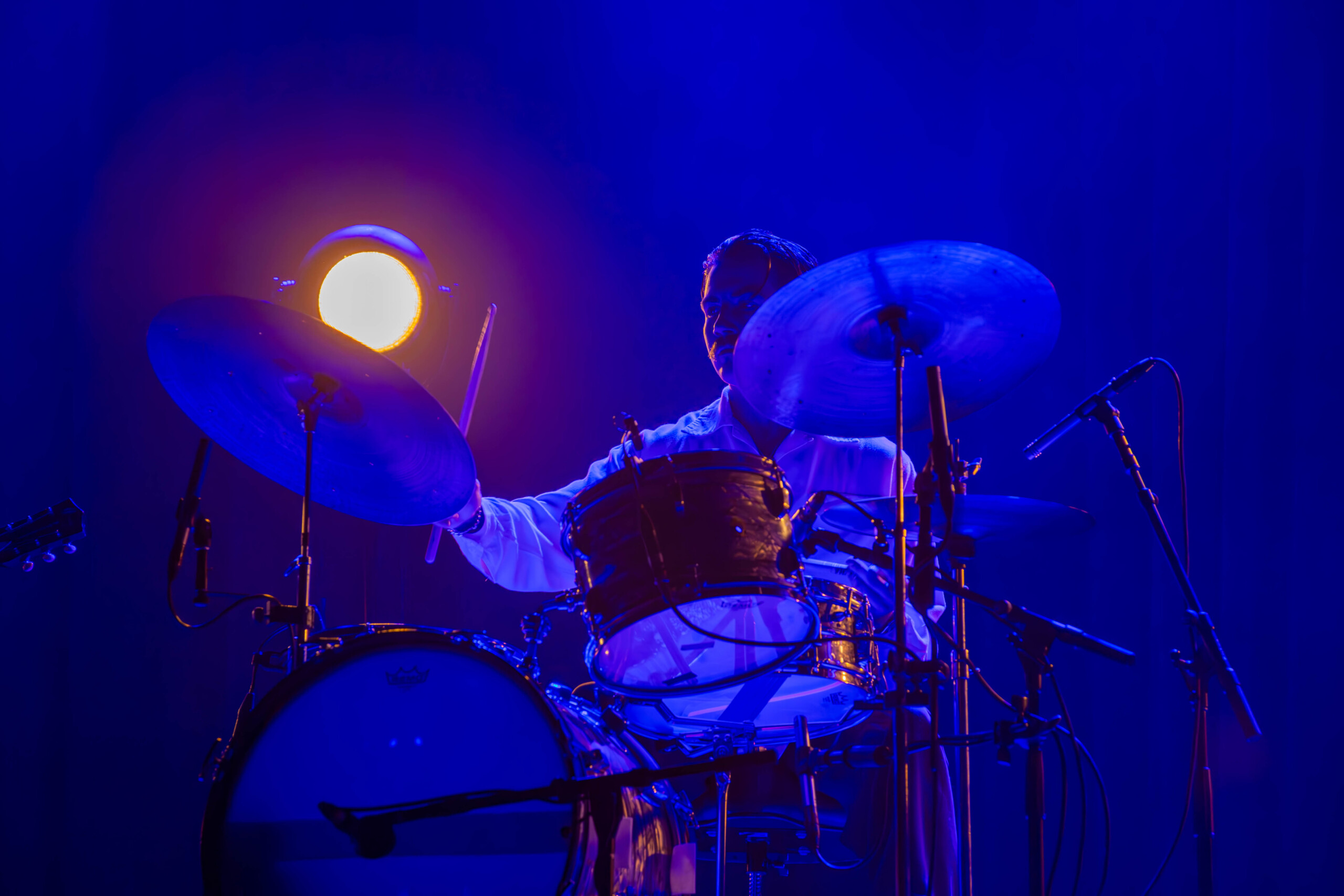 Thee Sacred Souls' drummer carefully taps the drums in front of heavy blue lighting.