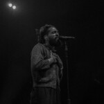 Thee Sacred Souls' lead singer stands before the mic in black and white.