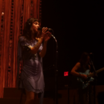 Clairo, onstage, singing in front of a red curtain.