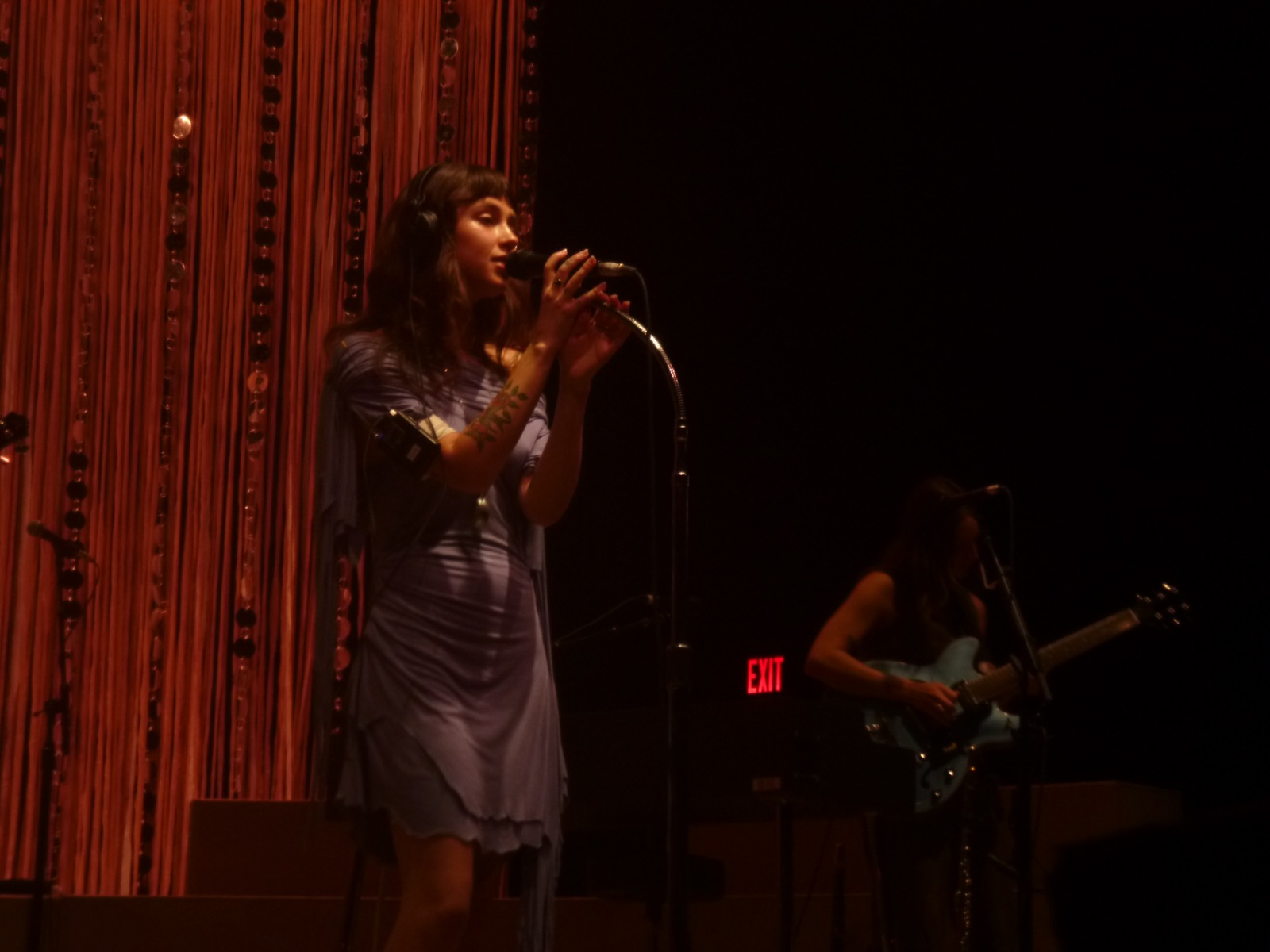 Clairo, onstage, singing in front of a red curtain.