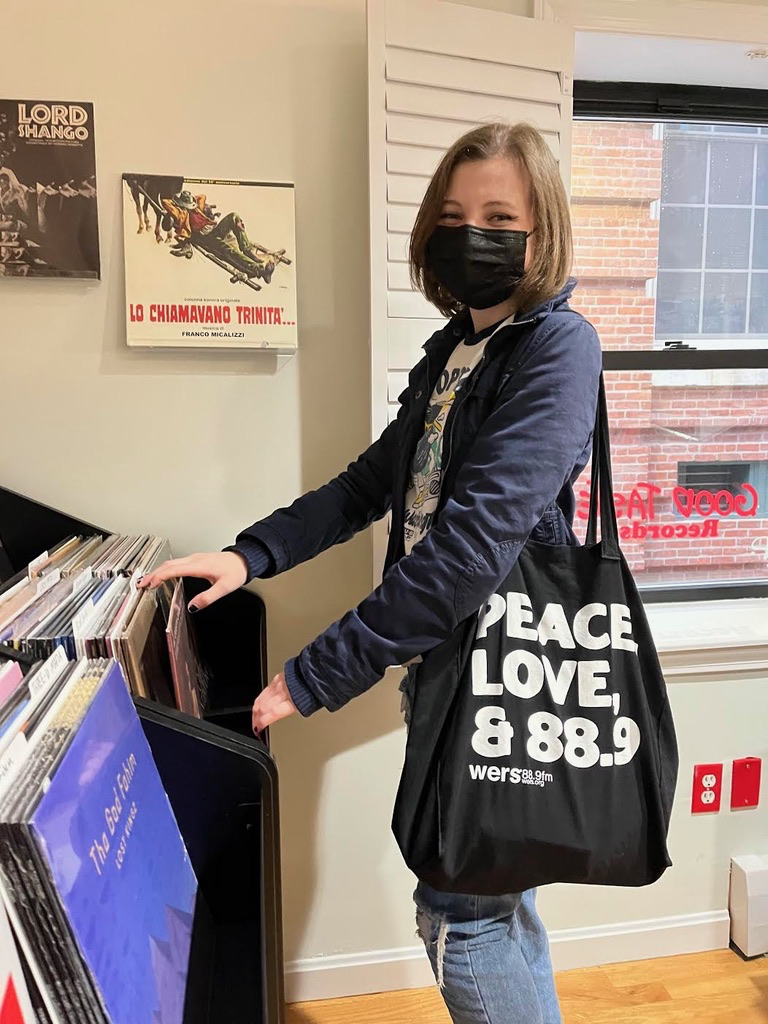 Nora at a record store with a black tote bag that reads "Peace, Love, and 88.9."