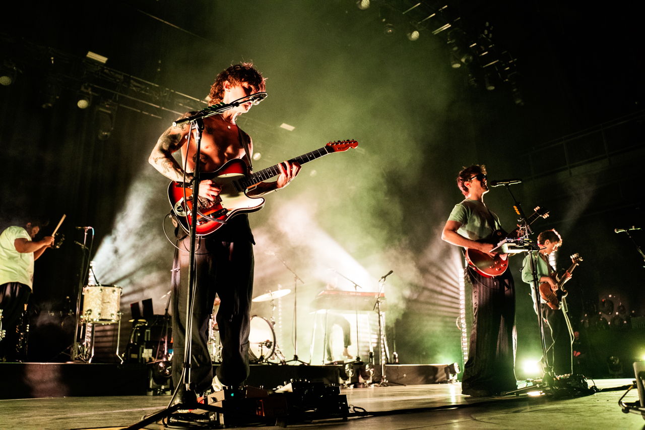 Hippo Campus rocks out in front of a green light while the bassist leaps in the air