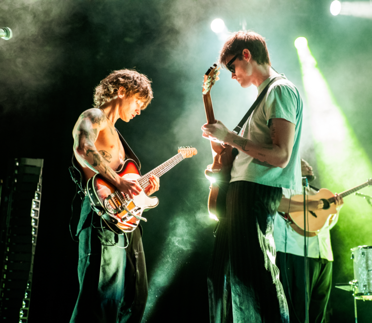 Two Hippo Campus Guitarists play while facing each other under light green lighting