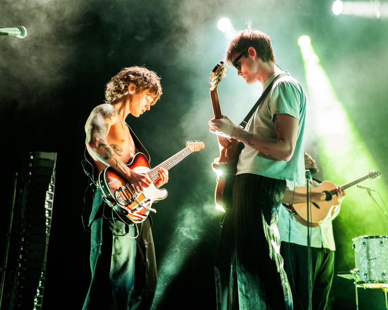 Two Hippo Campus Guitarists play while facing each other under light green lighting