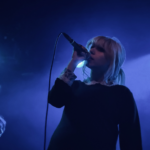 A blue light sines behind the Wunderhorse lead singer as she croons into the mcirophone.