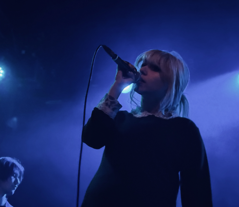 A blue light sines behind the Wunderhorse lead singer as she croons into the mcirophone.