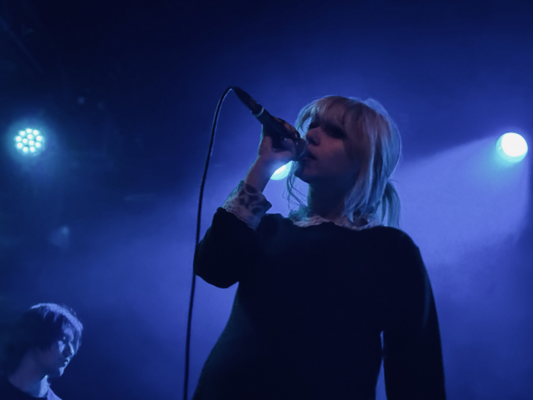 A blue light sines behind the Wunderhorse lead singer as she croons into the mcirophone.