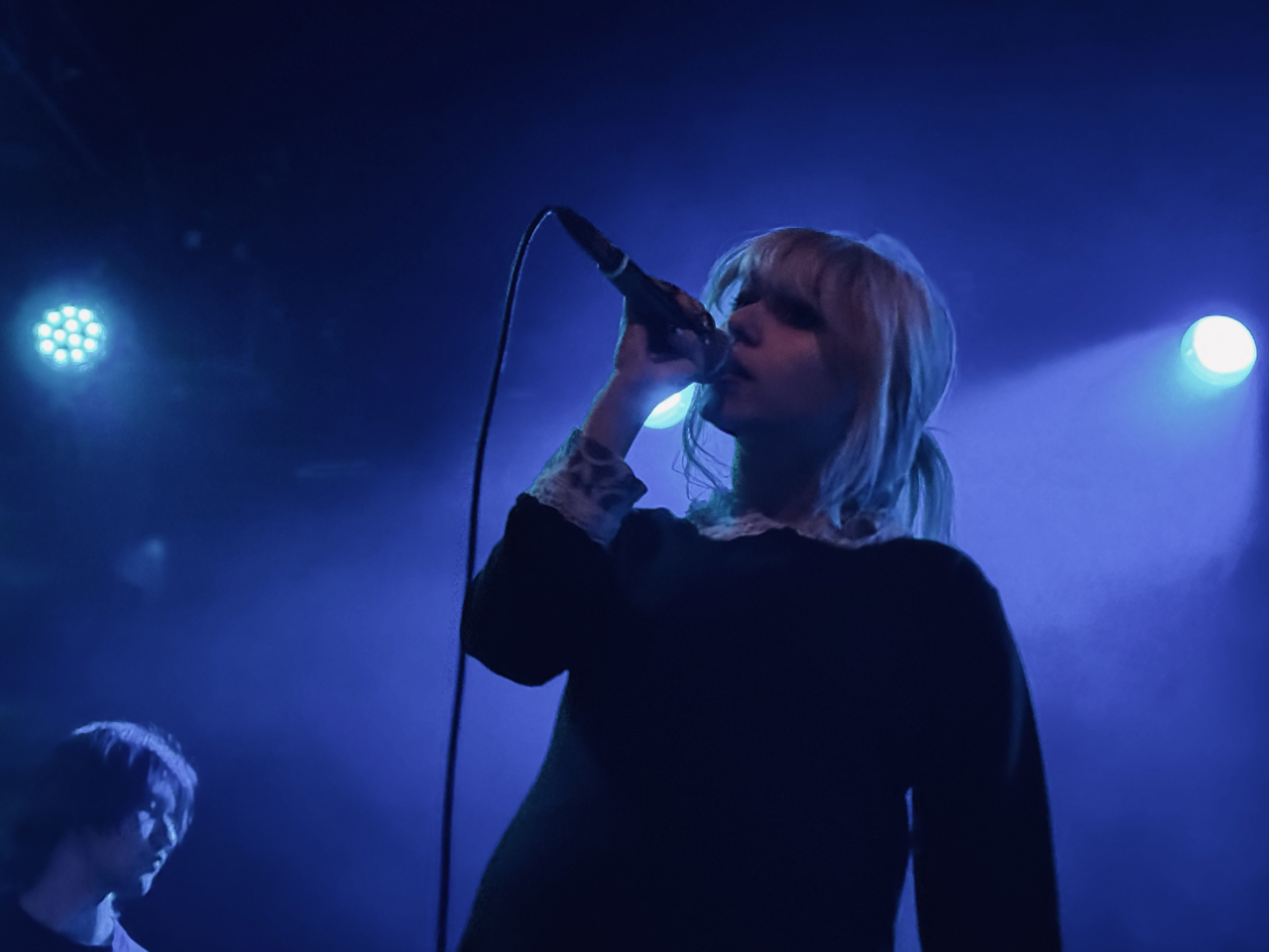 A blue light sines behind the Wunderhorse lead singer as she croons into the mcirophone.