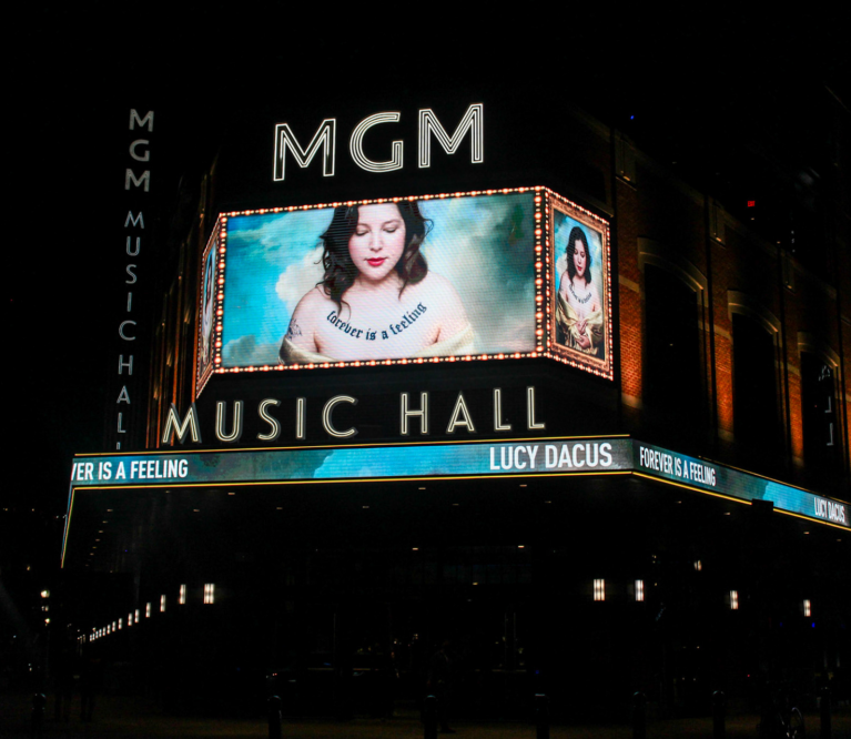 A photo of the outside of MGM Music Hall featuring Lucy Dacus on a large screen.