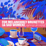 Multicolor foliage behind text that reads "For melancholy brunettes (and sad women)" and, in cursive, "Japanese Breakfast." A table is set under the text with coffee and cocktails.
