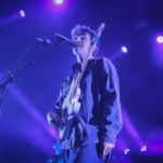 flipturn's lead singer, Dillon Basse, singing with his guitar onstage. Purple lighting overhead.